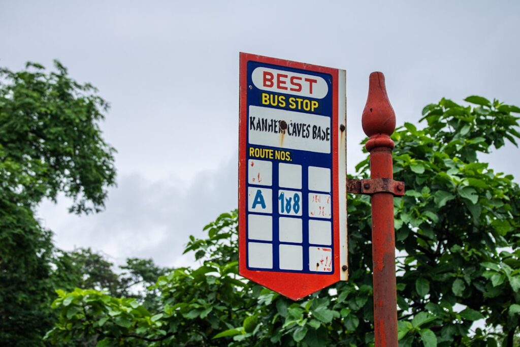 A bus stop sign stands outdoors in front of nature